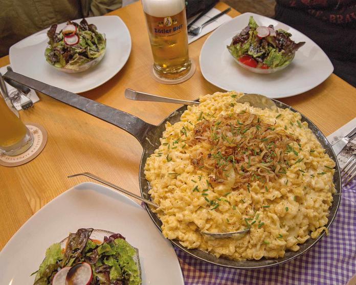 Eine große Schüssel allgäuer Kässpatzen mit Salatschüsseln nebendran 